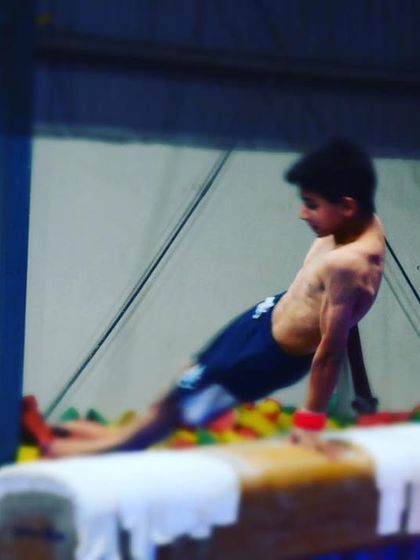 A young gymnast demonstrates incredible strength and form on the pommel horse, training over a foam pit for safety.