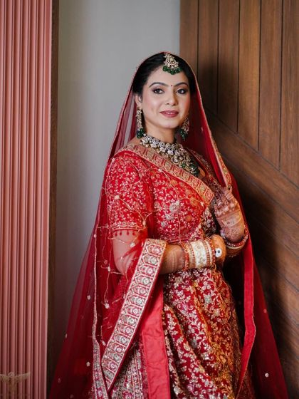 A full view of the bride's stunning red lehenga and flawless makeup. She looks confident and ready for her big day.
