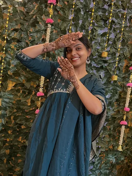 A happy client posing against a festive backdrop, showing off her beautiful mehndi. The design is perfect for a party or sangeet ceremony.
