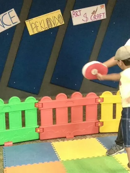 Making fitness fun. A young boy learns to punch a focus mitt during a summer camp, combining martial arts with other activities like dance and crafts.