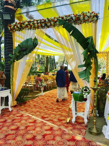 A traditional South Indian wedding entrance. The decor uses banana leaves, a floral-patterned carpet, and classic white pillars to create an authentic and welcoming feel.