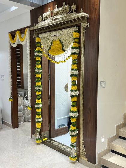 A beautifully decorated pooja room door, framed with traditional 'thomala' made of yellow and white flowers. This classic design brings a sense of sanctity and celebration to the housewarming ceremony.
