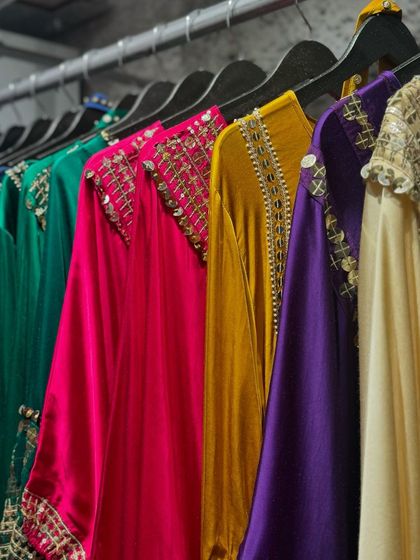 A rack of luxurious velvet tunics and kaftans in a rainbow of jewel tones, all featuring intricate neckline embroidery.