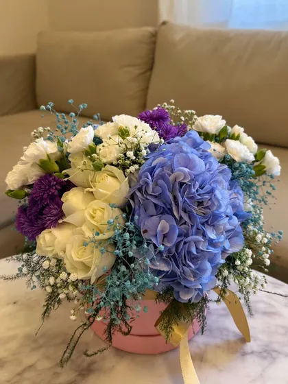 A closer look at the floral base for one of my hot air balloon gifts. This one features a stunning blue hydrangea surrounded by white and purple carnations and delicate baby's breath in a soft pink box.