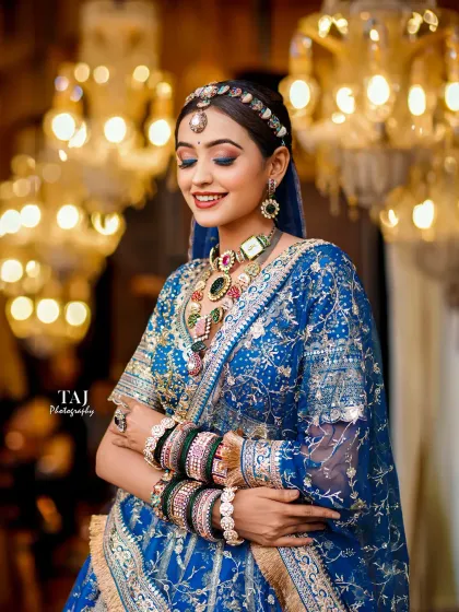 A joyful bride in a royal blue lehenga, surrounded by the warm glow of chandeliers. This shot is full of color, light, and happiness.