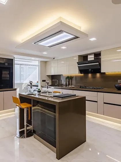 A spacious and modern kitchen with beige and cream glossy cabinets, a dark island, and top-of-the-line black appliances. The under-cabinet and ceiling lighting create a bright and welcoming space.