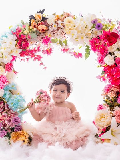 A beautiful portrait of a little girl named Anaisha, holding a bouquet and framed by a stunning floral arch.