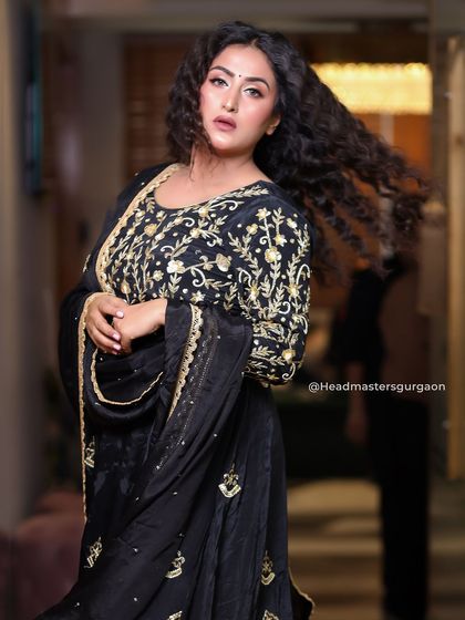 A dramatic and powerful look. The client's black and gold embroidered suit is paired with voluminous curls and a bold makeup look, perfect for making a statement.