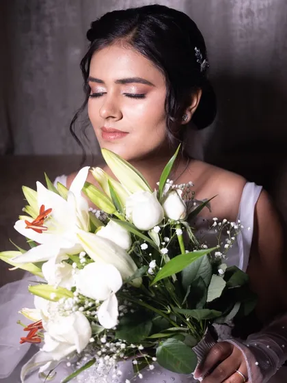 A serene portrait of bride Nisha, holding a bouquet of white lilies. Her makeup is soft, with a focus on flawless skin.