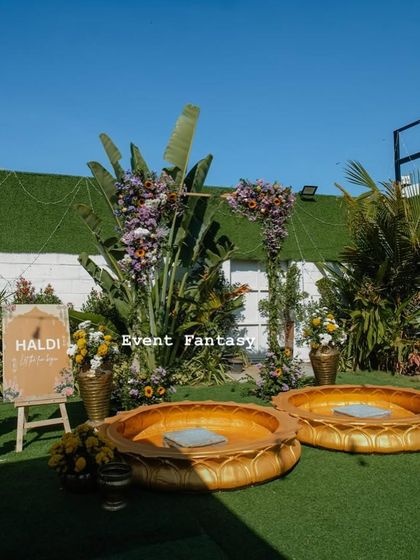 The Haldi setup in all its glory. The large golden lotus urlis are the centerpiece, complemented by a floral arch, brass props, and a personalized "Haldi" sign to welcome everyone.