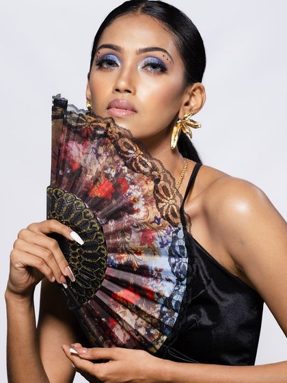 A close-up shot of a model with a Spanish-style fan, focusing on her nails and makeup.