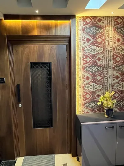 A grand entryway featuring a solid wood door with a decorative glass insert. The surrounding walls are adorned with patterned wallpaper and backlit panels, creating a warm and welcoming entrance.