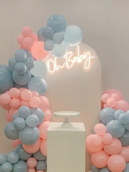 A simple and modern "Oh Baby" setup with a neon sign. The pastel pink and blue balloon garland against a white arch is perfect for a minimalist baby shower or gender reveal.