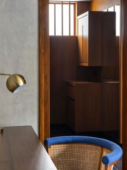 A detail of a study nook in the Brick House, where a brass lamp and a blue-upholstered chair provide a soft counterpoint to the raw concrete and wood finishes.