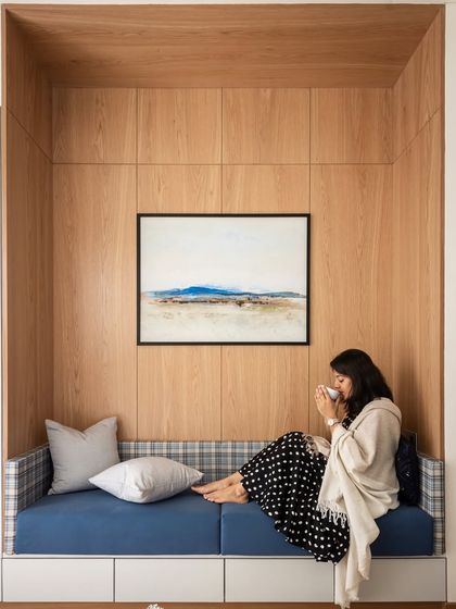 Across from the bed in another bedroom, we crafted this tranquil reading nook. The wall is paneled in a subtle oak veneer, creating a warm backdrop for the blue upholstery. An art piece above ties the design together, echoing the room’s rich hues.
