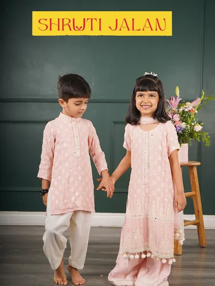 A sweet moment between a brother and sister in matching pale pink embroidered outfits. Her sharara set with pom-pom details complements his simple, elegant kurta.