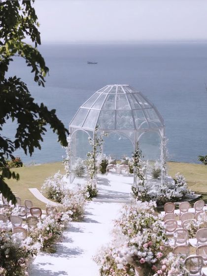 A stunning view of the glasshouse mandap for the 'Romantic Garden' wedding in Bali. Set on a cliffside overlooking the ocean, this minimalist yet breathtaking structure was designed to harmonize with the natural beauty of the location.