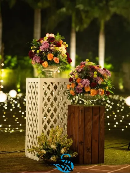A nighttime shot of our floral pedestals, with arrangements of colorful flowers set against a backdrop of twinkling fairy lights. This combination of rustic wood, classic lattice, and warm light creates a magical garden feel.