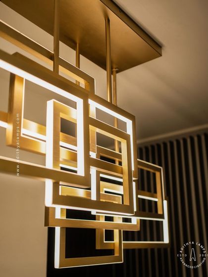 A multi-layered chandelier composed of intersecting rectangular frames with a brushed gold finish. The integrated LEDs cast a warm, ambient light, creating a dynamic and architectural statement piece for modern interiors.