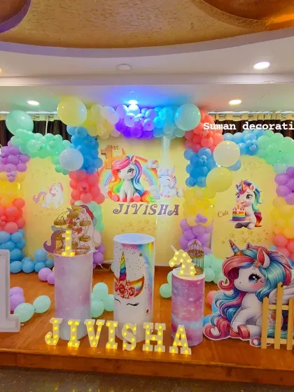A magical unicorn themed first birthday party. The setup is full of color, with a rainbow balloon arch, a themed backdrop, unicorn cutouts, and light-up letters for the name "JIVISHA".