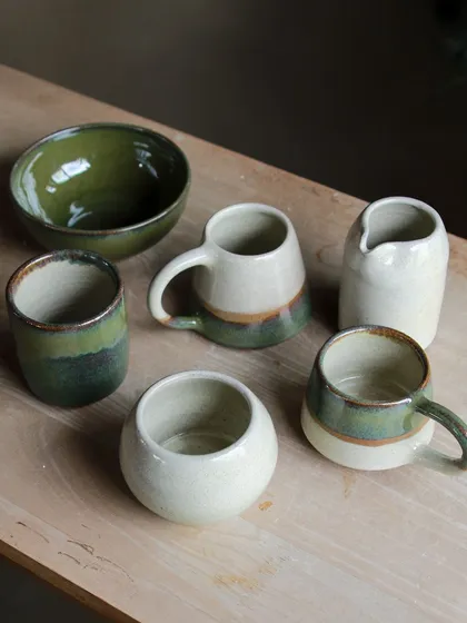 A selection of student pieces from the Apr-May cohort, featuring a beautiful range of green and cream glazes on mugs, bowls, and a pitcher.