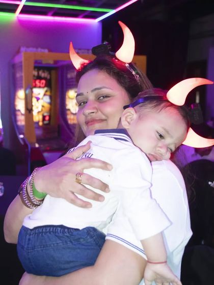 A fun, candid moment of a mother holding her sleepy child, both wearing playful light-up horns at a party.
