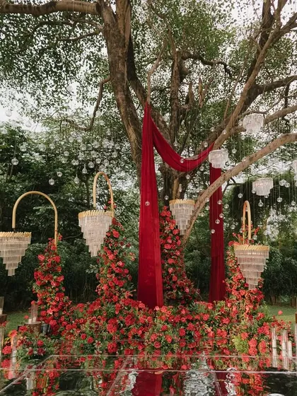 The decor elements coming together under a large tree, with red drapes, chandeliers, and floral towers creating a magical setting.