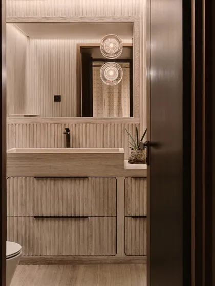 This powder room showcases our attention to texture and detail. The fluted wooden vanity and soft, ambient lighting create a warm and sophisticated space that feels both modern and timeless.