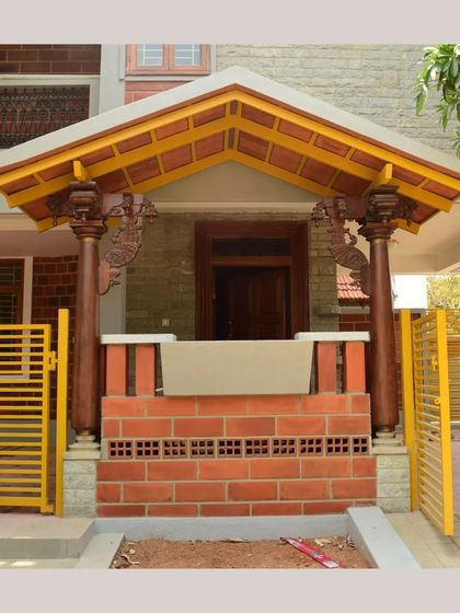 A traditional entrance porch with intricately carved wooden pillars and a sloping tiled roof, creating a warm and grand welcome.