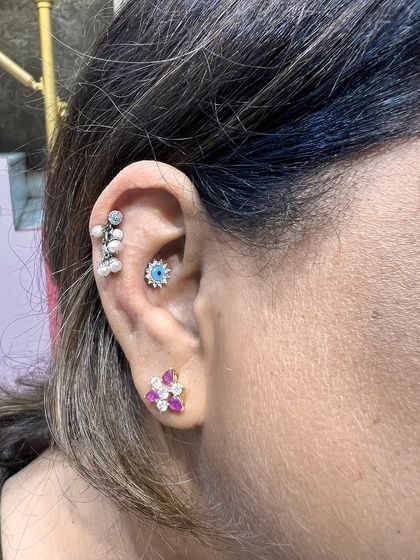 A colorful and unique stack with a pearl drop hanging, an evil eye stud, and a ruby floral lobe stud.