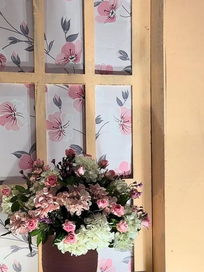 A detail shot of the custom decor for a Mehendi ceremony, showing a lovely floral arrangement in front of a window-pane style backdrop with a pink floral print.