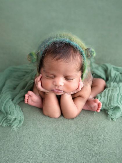 The classic "froggy pose" in a different light. This baby, wearing a fuzzy green bonnet, shows how this composite pose can be both adorable and completely safe.