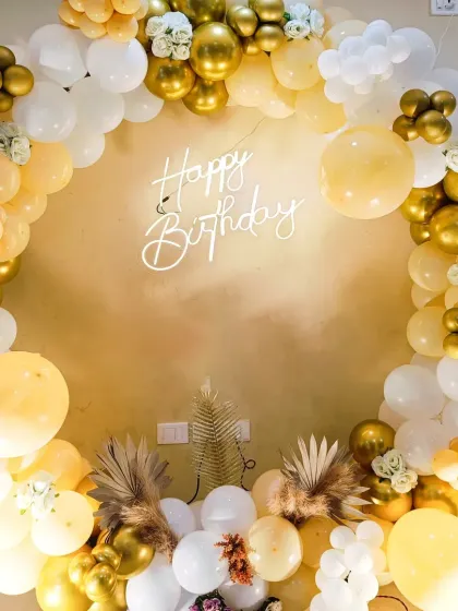 A full circular balloon arch in white and gold. This beautiful photo backdrop is accented with pampas grass and a 'Happy Birthday' neon sign for a chic, boho-glam look.