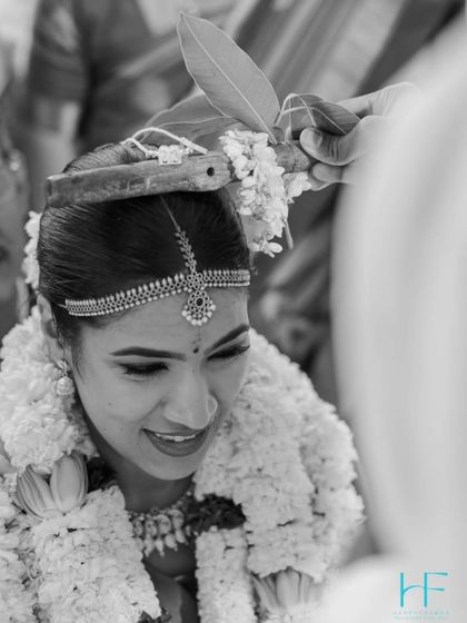 A close-up monochrome shot of a South Indian wedding ritual, focusing on the bride's happy expression and the delicate traditions.