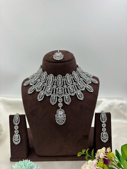 A full-coverage AD bridal set with a matching maang tikka. This silver-plated design is available in a wide range of colors like green, blue, pink, and white, making it a versatile choice for weddings.