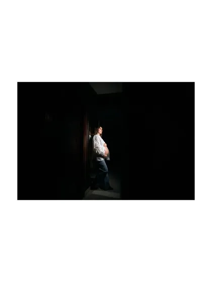 A powerful, low-key lighting portrait where the mom-to-be is highlighted against a dark background. This artistic shot emphasizes the silhouette of her baby bump.