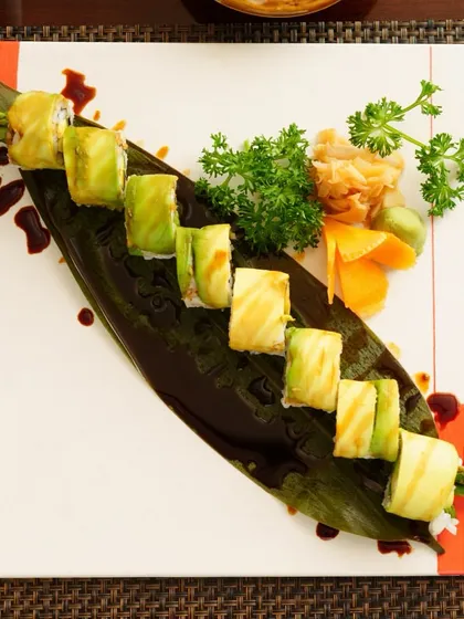 An overhead view of our legendary Dragon Roll, beautifully presented on a leaf-shaped platter. The layers of avocado and rich sauce make this a truly unforgettable dish.