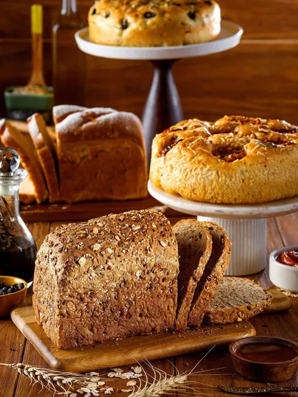 A beautiful spread of various freshly baked breads and cakes. This shot showcases the variety available at a bakery, from multigrain loaves to sweet focaccia, arranged to look like a generous, welcoming feast.