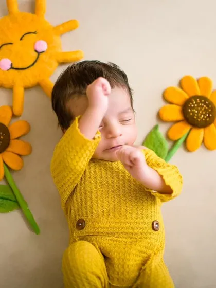A sweet flat-lay photo of a newborn in a yellow outfit, sleeping next to felt sun and sunflower props.