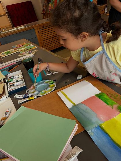 A young artist at our summer camp is completely focused as she paints sections of her project. We provide all the materials, including quality paints and paper, so students can fully explore their creativity.