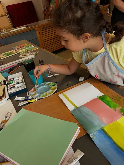 A young artist uses a palette to mix watercolors for her book project, a fundamental skill we teach in our workshops.