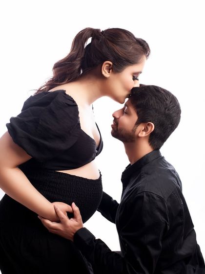 An intimate and loving gesture between partners. The gentle forehead kiss and the coordinated black outfits create a powerful and emotional couple portrait against a clean white background.