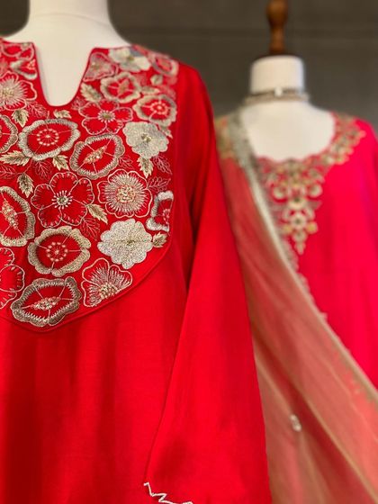 A close-up of a bright red kurta with beautiful floral embroidery around the neckline in white and gold thread.