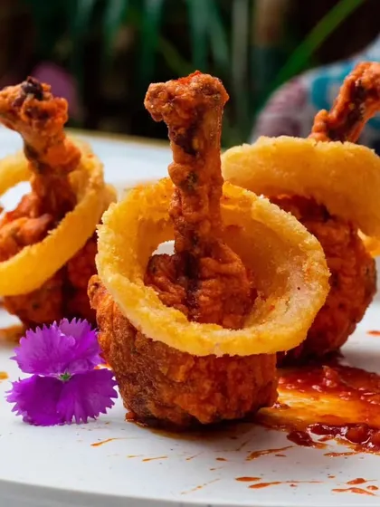 A culinary masterpiece. Our version of chicken lollipops, presented with a crispy onion ring, showcasing creative and playful plating.