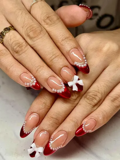 A festive red French manicure with pearl borders and 3D white bows. This is a perfect example of holiday-themed nail art that clients love.