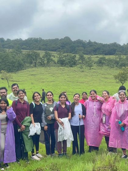 A happy group of trekkers in their rain gear, surrounded by the lush green meadows typical of a Western Ghats monsoon trek.