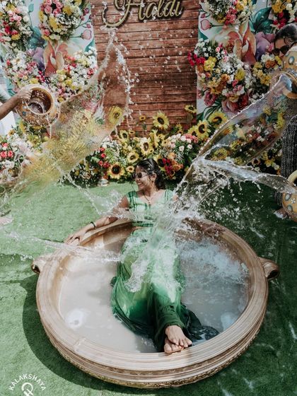 A dramatic splash shot of the bride during her Haldi ceremony, seated in a large decorative vessel.