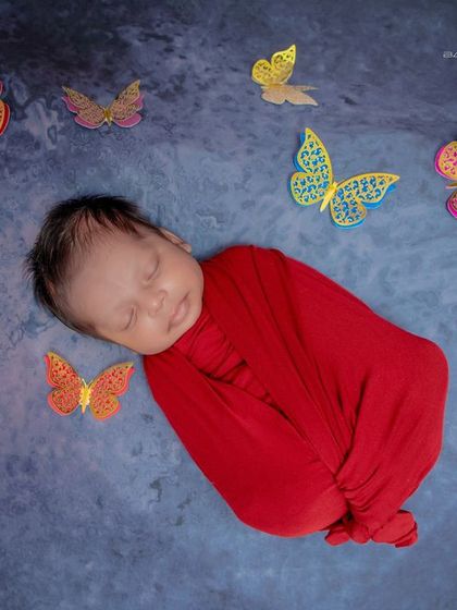 A little butterfly. The simple red swaddle makes this baby look like a caterpillar in a cocoon, ready to transform, with butterflies fluttering nearby.