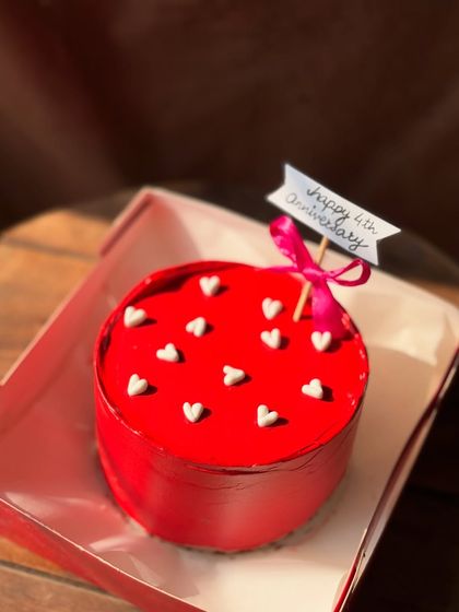 A vibrant red bento cake celebrating a 4th anniversary. Dotted with tiny white hearts and topped with a "Happy 4th Anniversary" flag, it’s a simple and sweet way to celebrate a milestone.