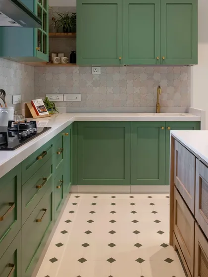 This kitchen has a quiet, cheerful personality. The soft green shaker-style cabinets are paired with a patterned backsplash and floor tiles, creating a gentle rhythm. The wooden island with its integrated storage adds a warm, functional centerpiece.